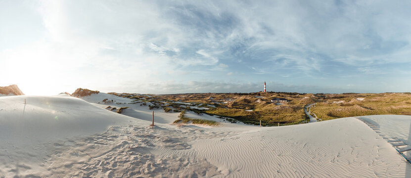 Panoramic view from lookout sand dune on North Sea coastal landscape with red and white lighthouse in distance.