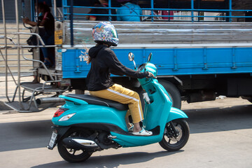 A woman rides a motorcycle on the street next to a truck carrying people,Thailand.