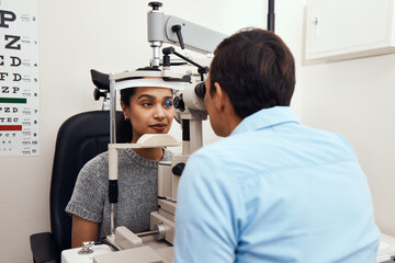 Fototapeta na wymiar Cant see Come to me. Shot of a young woman getting her eyes examined with a slit lamp by an optometrist.