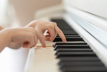 the hands of a young boy play on the keys of a white piano close-up in a bright room