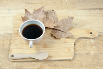Coffee cup on wood table with dry leaves and wooden spoon