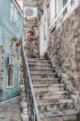 Vertical geometric vintage background with staircase outside a stone building in the Old Town Stari Grad in Budva, Montenegro. Light beige-blue architectural background of a narrow street