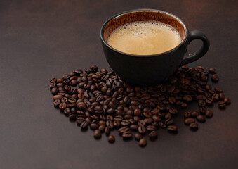 Large cup of hot black coffee with raw beans on brown background.