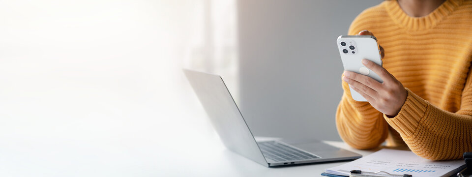 Asian woman business owner holding mobile phone View ordering information through the online website to prepare for packing in parcel boxes and delivering to customers.