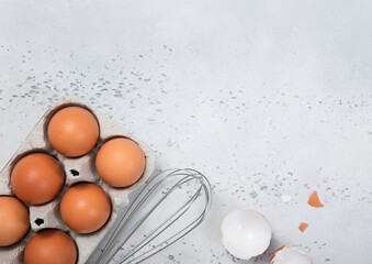 Tray with organic brown eggs with yolk,whisk and shell on light kitchen background