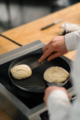A professional chef in the kitchen of a restaurant prepares pancakes for breakfast. Culinary recipe Frying pan on the stove
