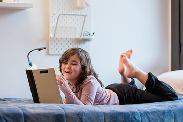 Happy little girl reading book on bed