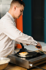 Obraz na płótnie Canvas A professional chef in the kitchen of a restaurant prepares pancakes for breakfast. Culinary recipe Frying pan on the stove