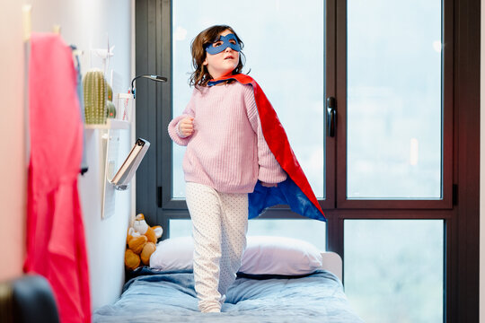 Cute little girl pretending to be superhero in bedroom