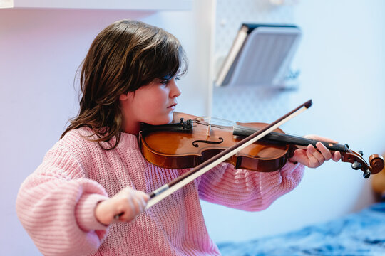 Cute child practicing violin in bedroom