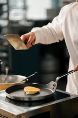 The cook prepares pancakes or pancakes for breakfast in a professional kitchen the pancake is removed from the pan