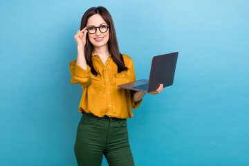 Photo of smile young lady brunette hair wear yellow shirt green pants fix specs hold computer boss working office isolated on blue color background