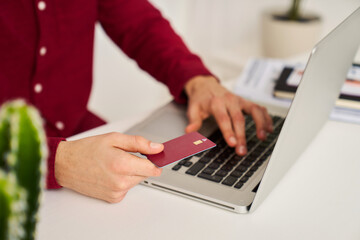 Anonymous man with credit card using laptop at home