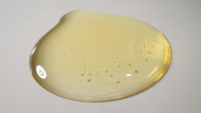 Drops of fresh jojoba oil falling down spreading on white plain surface. Transparent golden liquid with small bubbles. Skincare product macro