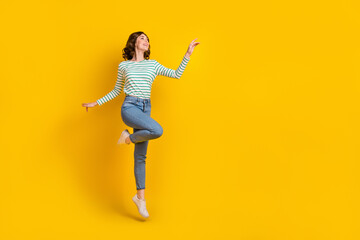 Fototapeta na wymiar Full size photo of friendly gorgeous woman dressed striped shirt jeans shoes flying look empty space isolated on yellow color background