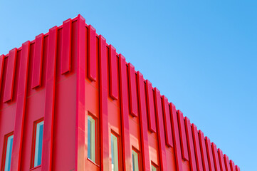 Fototapeta premium Modern red architectural office building. Metal sheets covering the exterior of the structure. Modern futuristic style building. Clear sky at the background. Unique building.