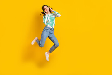 Fototapeta na wymiar Full size photo of good mood gorgeous woman dressed striped shirt jeans shoes arms touching headphones isolated on yellow color background