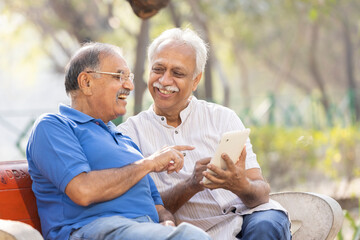 Fototapeta premium Two senior male friends using digital tablet at pake.