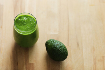 Green organic smoothie made from freshly prepared raw vegetables in a glass and whole avocado on...
