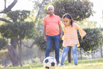 Little girl with grandfather playing football in park