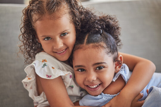 Happy, smile and portrait of sisters hugging while sitting on a sofa in the living room at the family home. Happiness, love and girl siblings from puerto rico bonding while relaxing on couch together