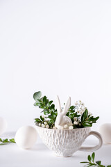 Easter egg and spring flowers  with bunny in tea cup on white background. Creative Easter holiday concept. Minimal greeting card with copy space for text.