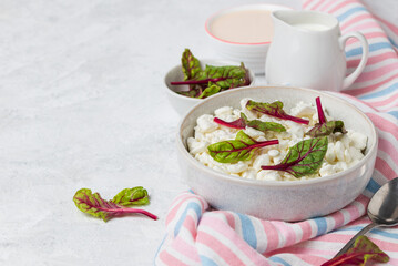 Breakfast with natural cottage cheese with green chard leaves in bowl and creamer with milk on pink...