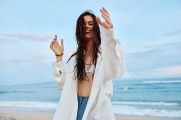 Fototapeta na wymiar Brunette woman with long hair in a white shirt and shorts smile and happiness walking on the beach and having fun smile with teeth pulling hands into the camera selfies ocean, vacation summer travel