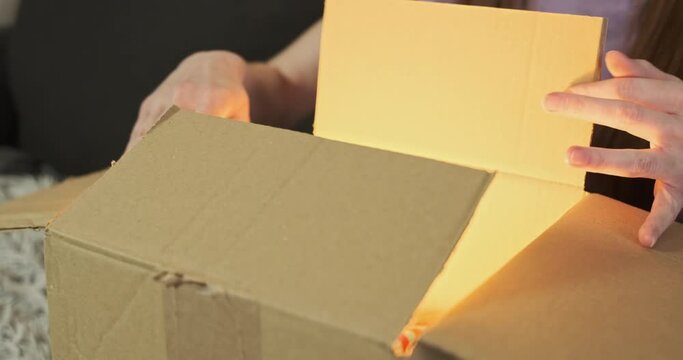 Women's hands take out an old multi-colored sock from cardboard box. Bright light comes from inside the box. Side view, close-up. Concept of a strange gift, high expectations.