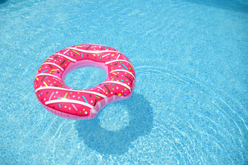 Pink doughnut pool float floating in a bright blue swimming pool
