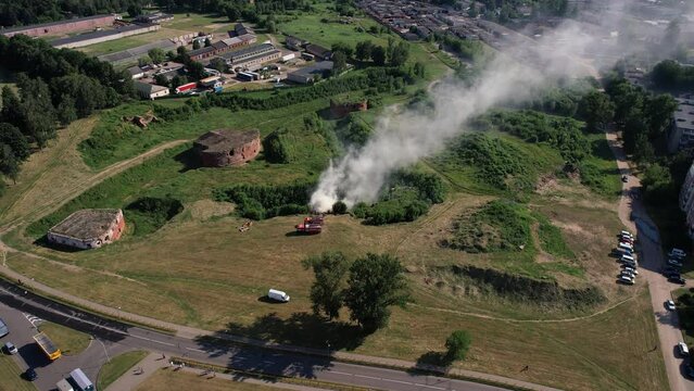 Aerial view of column of smoke from burning grass near the city's old fortress and fire trucks on wasteland