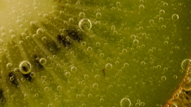 Ripe kiwi slices in air bubbles on an orange background.