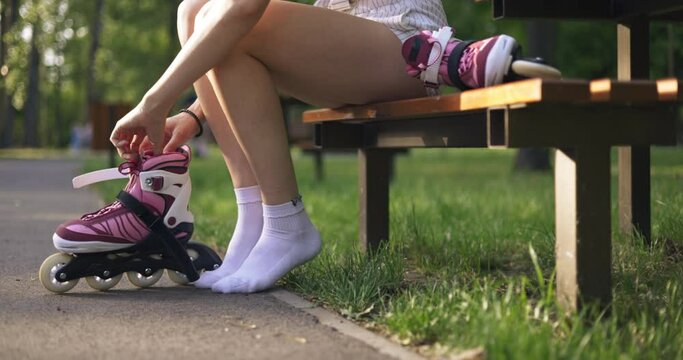 A woman sitting on a bench puts her foot into a rollerblade