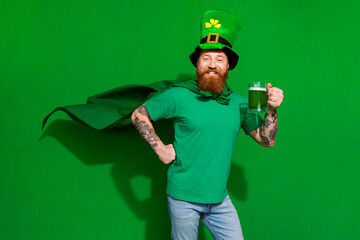 Photo of confident funky guy dressed t-shirt shamrock hat cape drinking beer isolated green color...