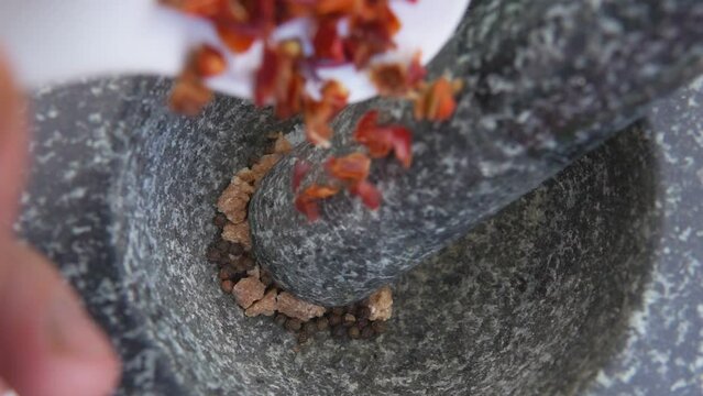 Super close-up of spicy dried chili pepper falling into the grey stone mortar 
