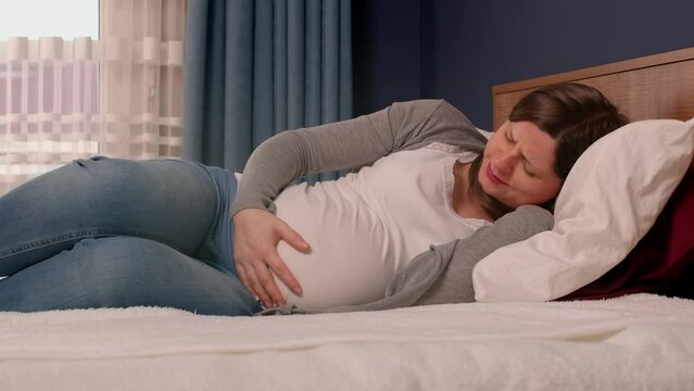 Pregnant woman with big belly in the bedroom, contractions begin, she feels pain. Last month's pregnancy, starting of childbirth.
