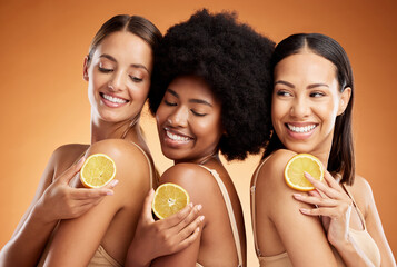 Skincare, diversity and women, beauty and lemon for health, wellness and nutrition on orange studio background. Friends, smile and happy models with fruit for vitamin c, healthy or glowing skin.