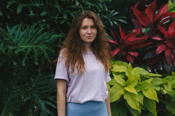 portrait of young girl on a green, natural background, eco friendly woman in a tropical park or jungle, positive lady enjoys walk at garden at summer day 