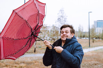 Shocked male man fool around with umbrella in city park, strong storm wind, rain and bad weather....