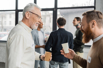 Smiling men with paper cups talking during alcoholics meeting in recovery center.