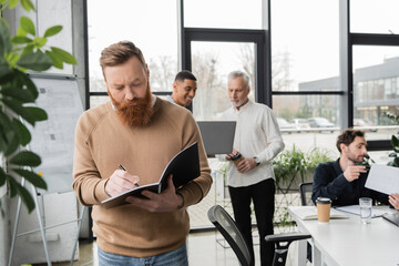 Bearded businessman writing on notebook during training in office.