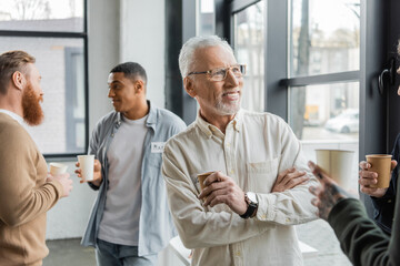 Fototapeta premium Smiling mature man holding paper cup during alcoholics meeting in recovery center.