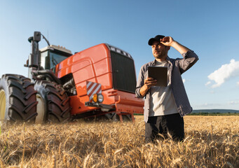 Farmer with a digital tablet on the background of an agricultural tractor