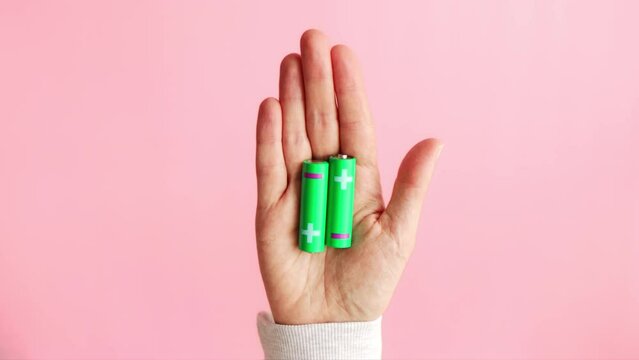 Green alkaline batteries AA type rechargeable accumulators in hand on pink background. Battery recycling and renewable energy concept.	