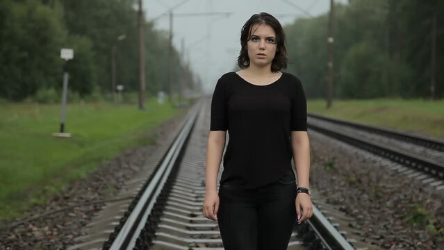 A girl walks barefoot on a railroad track. Dramatic background of suicidal thoughts. Desperate woman wants to commit suicide on the railroad. Young girl with psychological or mental problems.