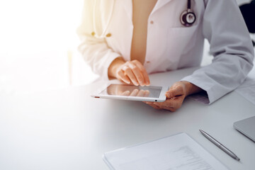 Unknown doctor woman sitting and writing notes at the desk in clinic or hospital office, close up.  Medicine concept.