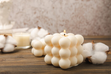 Soy wax candle on a textured table. Interior decor with a handmade burning candle and cotton flowers. Hygge home decoration concept and aromatherapy. Comfort at home.Place for text. Design