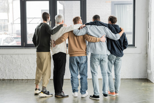 Back view of interracial men hugging during anonymous alcoholics meeting in rehab center.