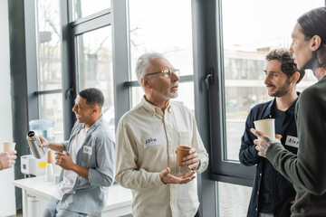 Mature man with alcohol addiction holding paper cup and talking to people in recovery center.