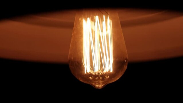 L&acirc;mpada de filamento de carbono emitindo luz amarela por dentro do abajur e girando r&aacute;pido